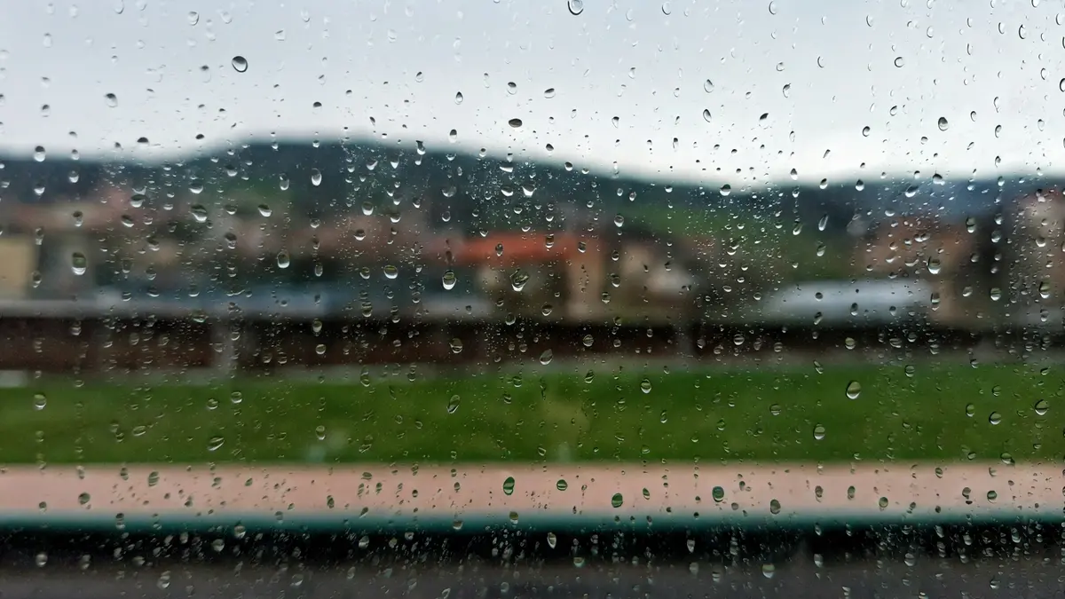 Euri-tantak leiho batean, atzealdean Euskadiko udaberriko paisaia lausoa duena.