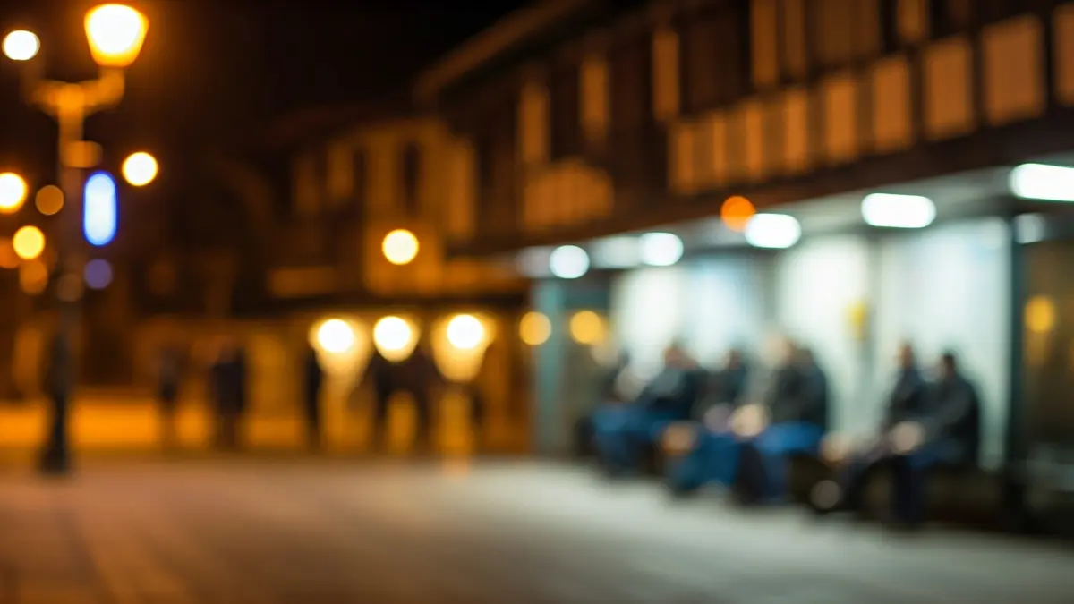 Imagen genérica de una parada de autobús al anochecer, con algunas figuras indistintas esperando.
