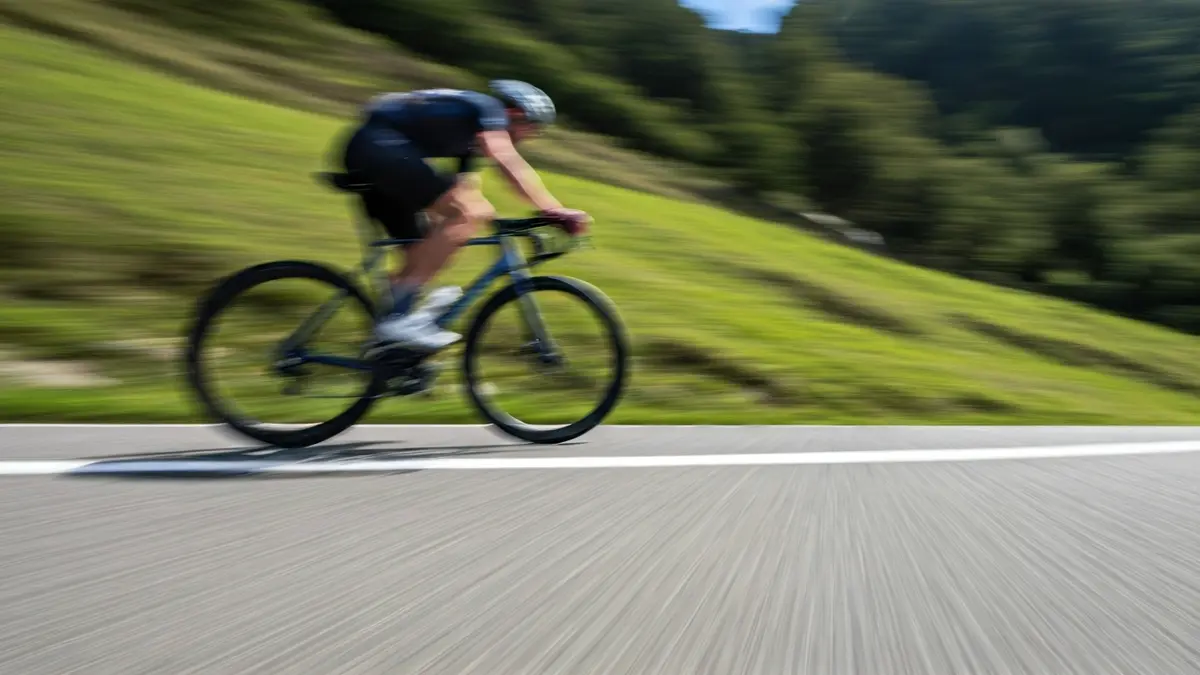 Txirrindulari baten hankak aldapa gogor batean pedalei eragiten, atzealdean Euskal Herriko paisaia berdeak.