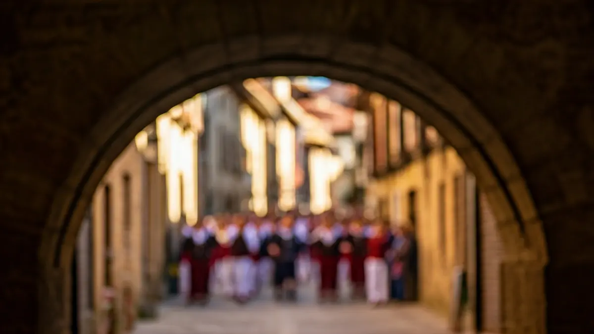 Image of a traditional stone archway in Balmaseda's old town, with blurred figures in the background suggesting a procession.