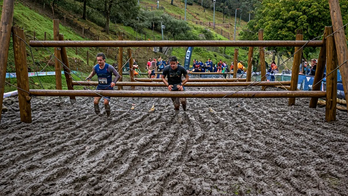 Imagen genérica de un circuito de obstáculos con barro y estructuras de madera, corredores difuminados al fondo.