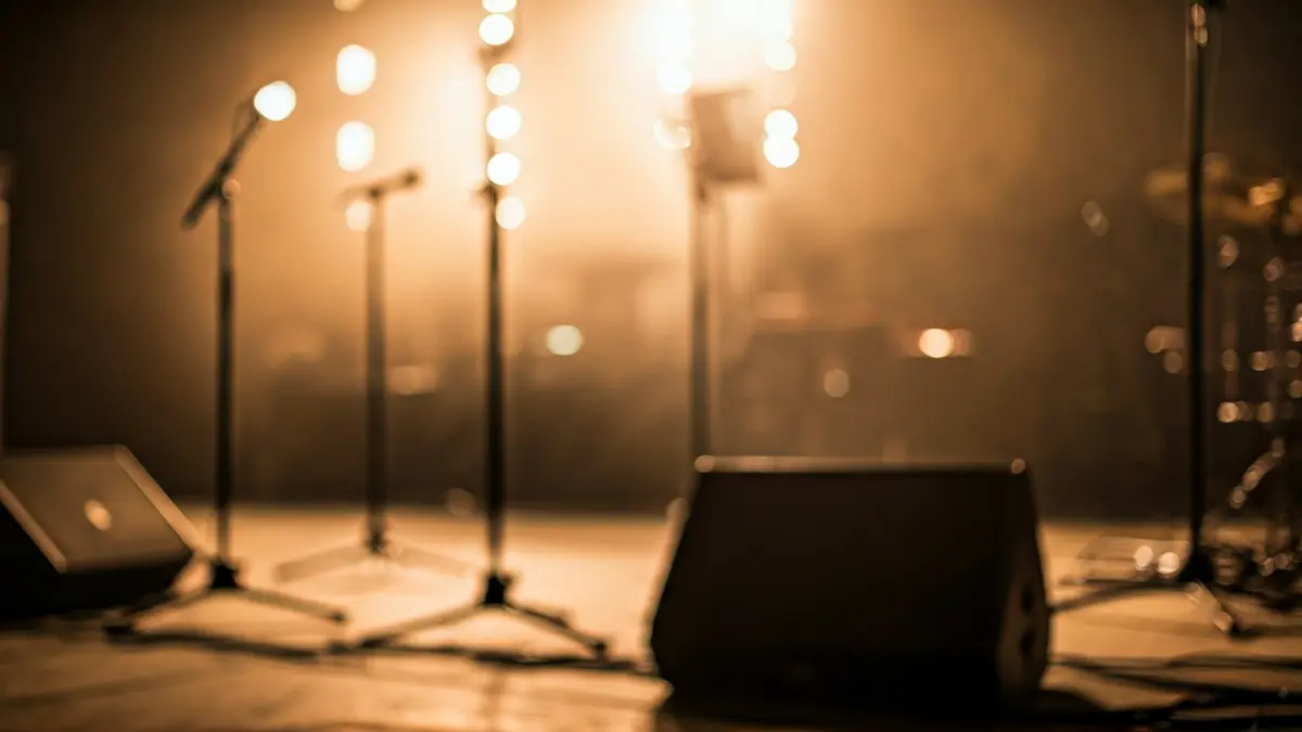 Generic image of an empty concert hall stage with microphone stands and musical instruments.
