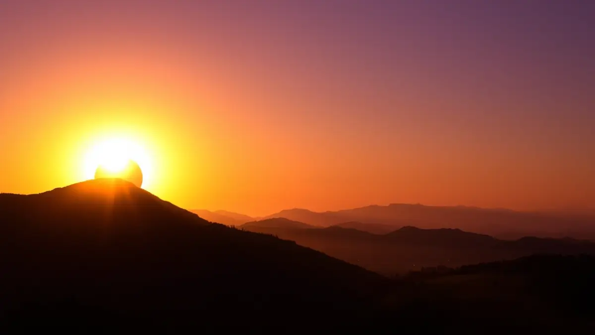 Imagen dramática de un eclipse solar sobre un paisaje montañoso al atardecer.