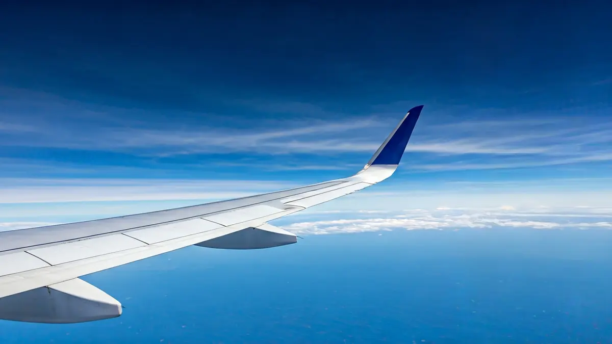 Imagen genérica de un ala de avión contra un cielo azul claro, simbolizando el aumento de los costes de los viajes.