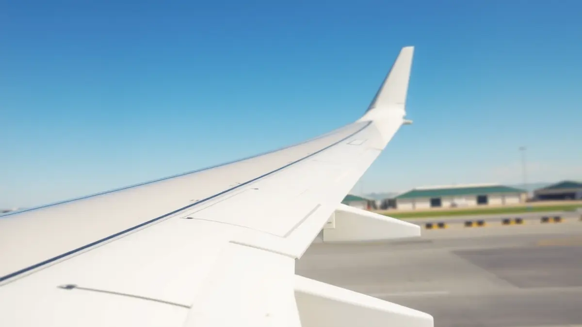 Imagen genérica del ala de un avión con un terminal de aeropuerto difuminado al fondo.