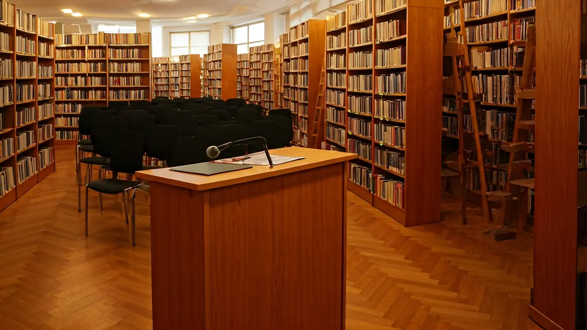 Imagen genérica del interior de una biblioteca con estanterías y un micrófono.