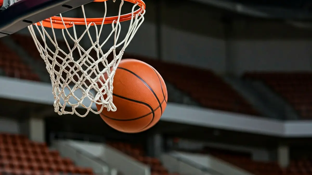 Generic image of a basketball net with a ball passing through, in a brightly lit sports arena.