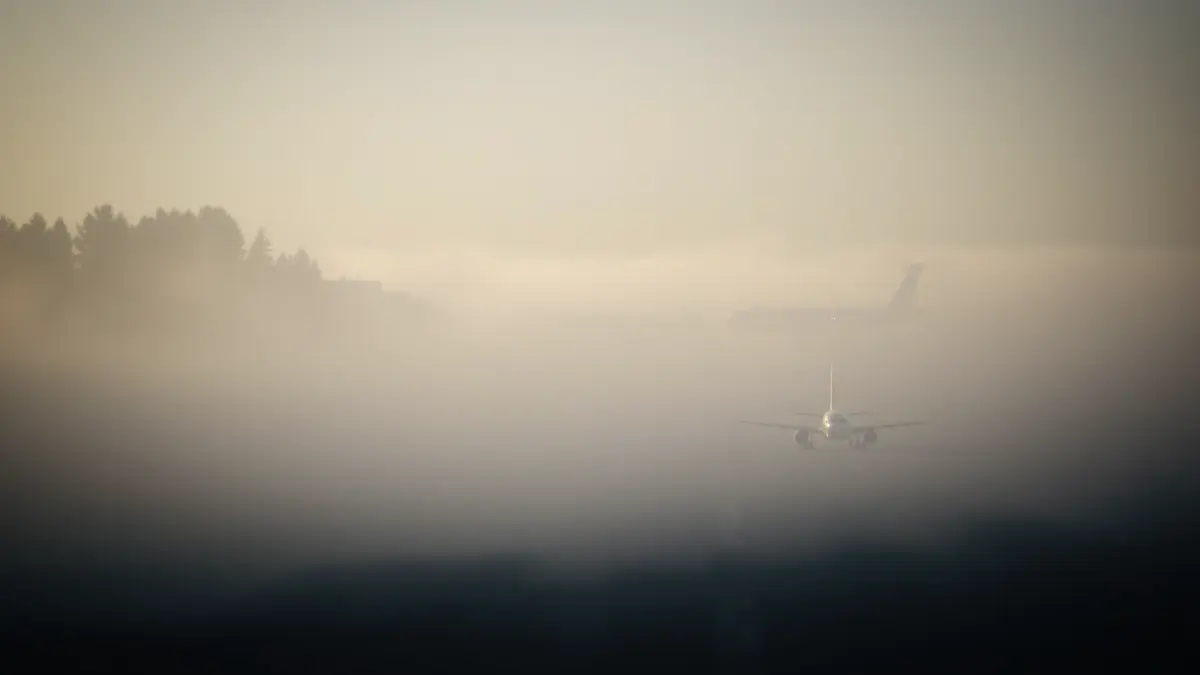Generic image of an airport runway covered in dense fog, with a blurred airplane silhouette in the distance.