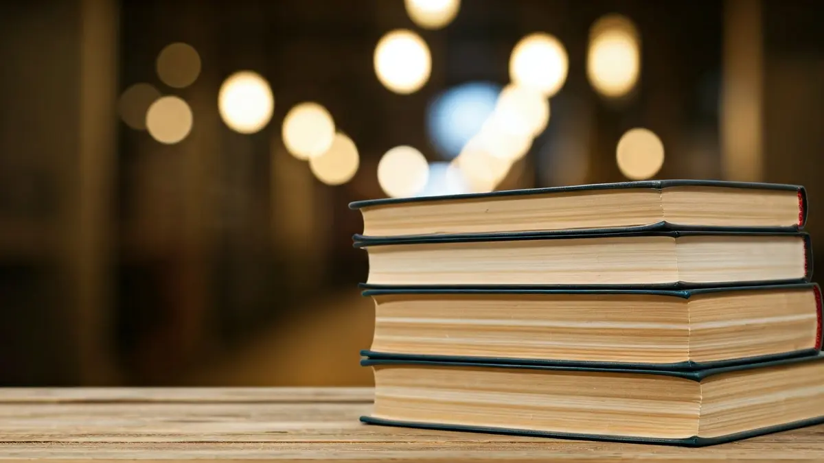 Imagen genérica de una pila de libros sobre una mesa de madera, con un fondo borroso.