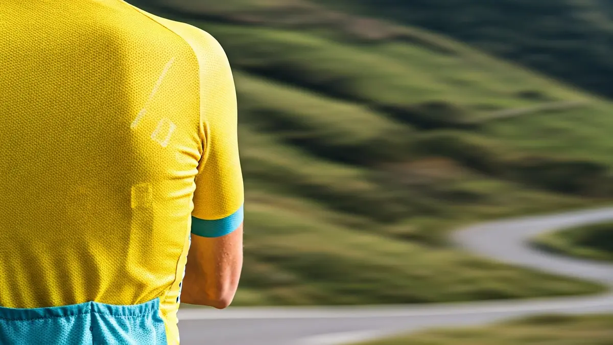 Primer plano de un maillot de ciclista amarillo con un fondo borroso de una carretera sinuosa y colinas verdes.