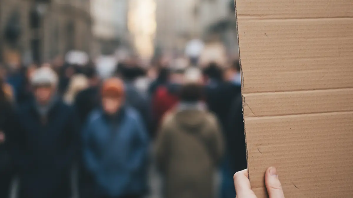 Generic image of a protest, with a sign held by a hand and a blurred crowd in the background.