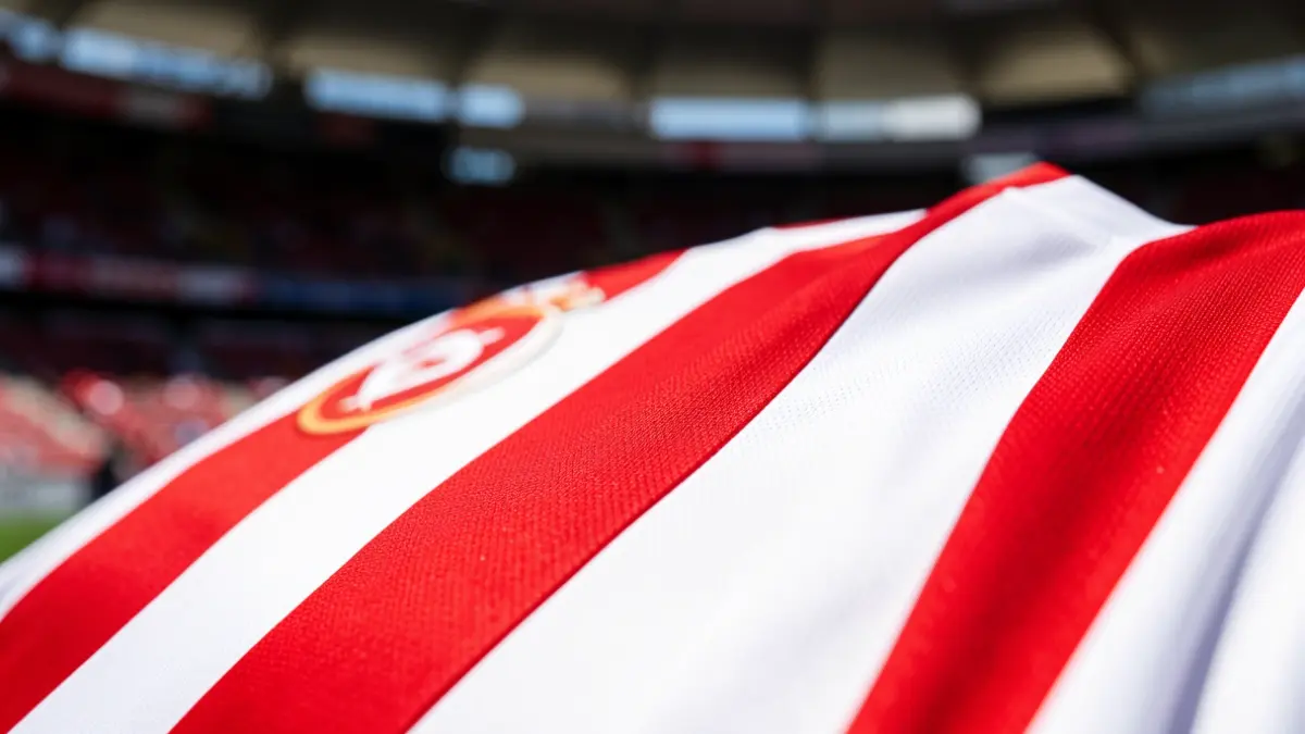 Imagen genérica del detalle de una camiseta del Athletic Club a rayas rojas y blancas, con el fondo difuminado del estadio de San Mamés.