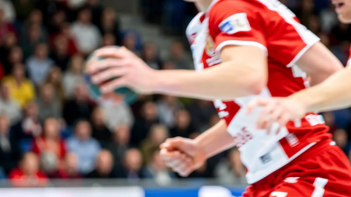 Irudi generikoa: Eskubaloi jokalari baten eskuak mugimenduan, kamiseta gorri-zuria jantzita, estadio eta zaleen atzealde lausoarekin.