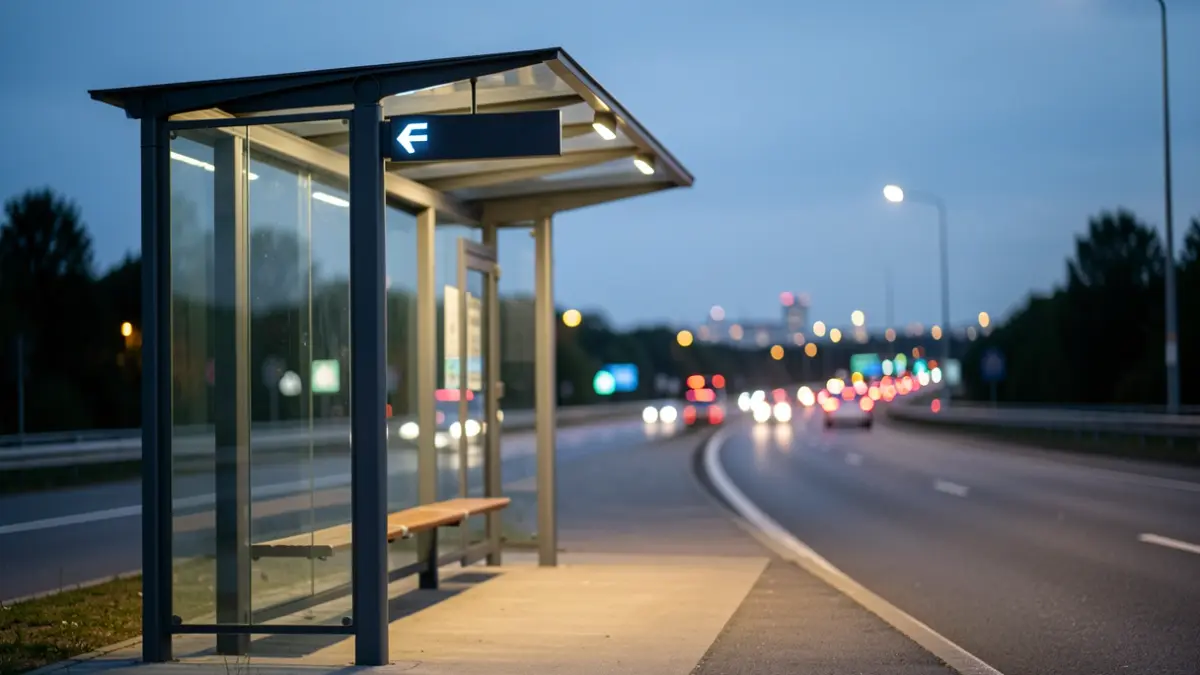 A modern bus stop shelter, illuminated at dusk, with distant city lights.