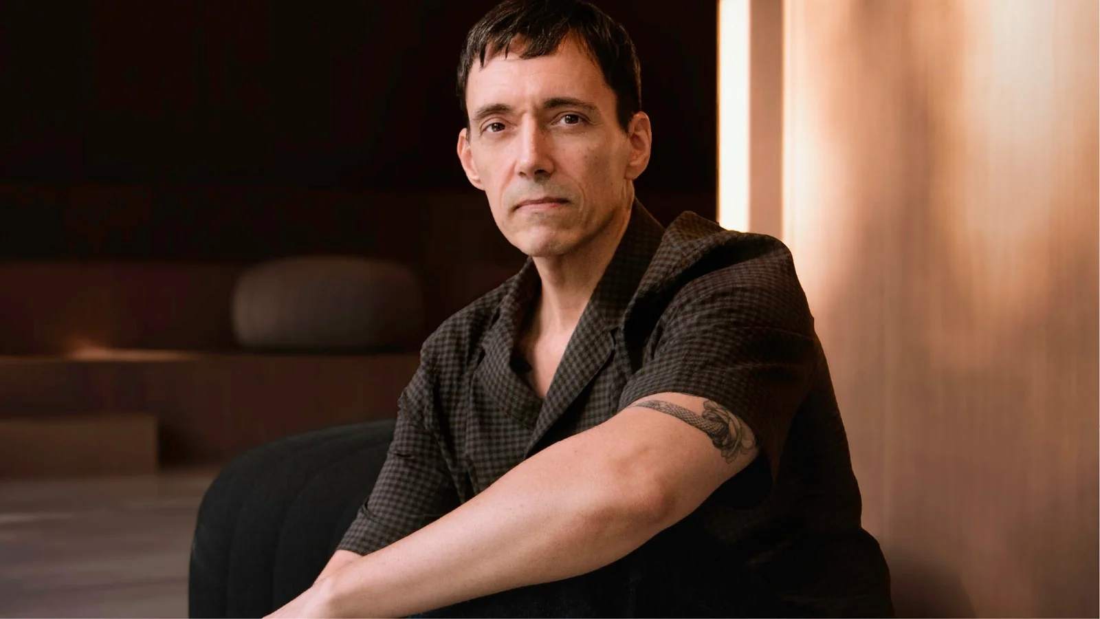 Portrait of designer Caco Martín sitting on a dark sofa.