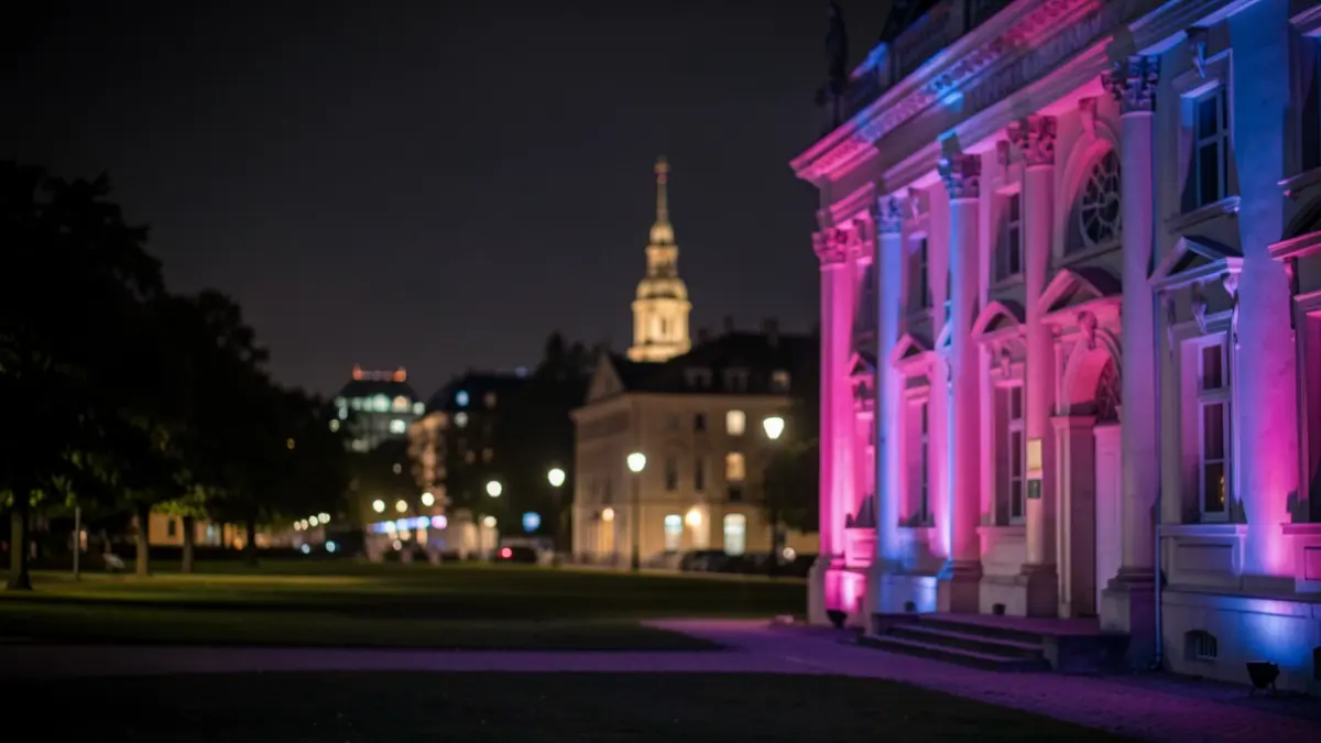Generic image: public building facade illuminated in pink and blue light at night, with a blurred background of a park and other illuminated structures, creating a somber and supportive atmosphere.